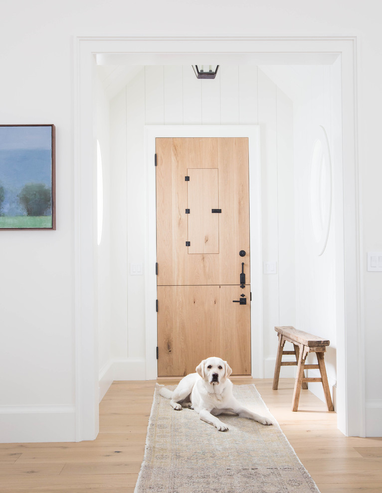 Réalisation d'un hall d'entrée champêtre avec un mur blanc, un sol en bois brun, une porte simple, une porte en bois brun et un sol marron.