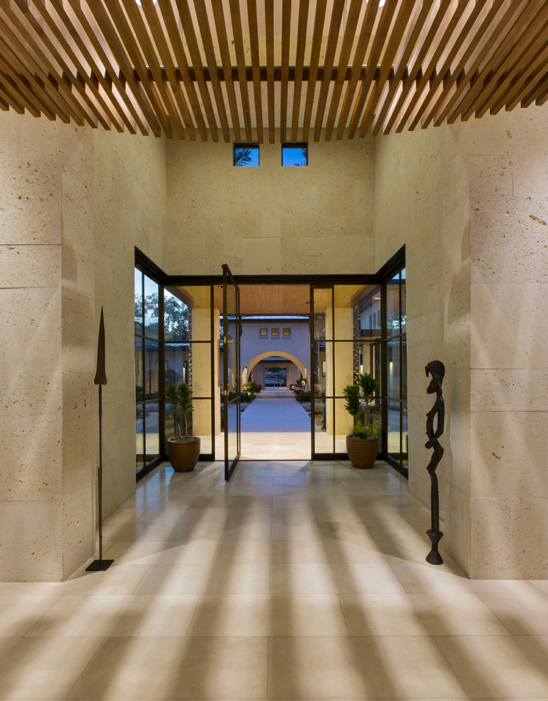 Idée de décoration pour un grand hall d'entrée design avec un mur beige, un sol en travertin, une porte pivot et une porte métallisée.