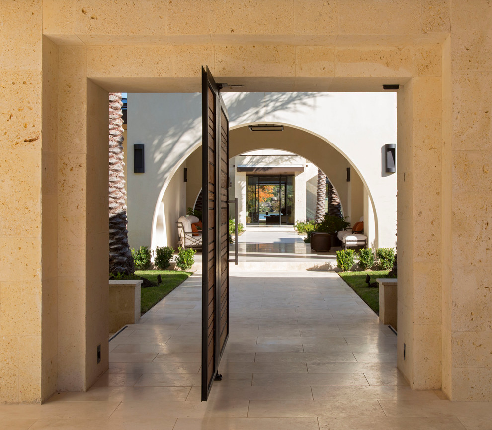 Cette image montre une grande porte d'entrée design avec un mur beige, un sol en calcaire, une porte pivot et une porte métallisée.