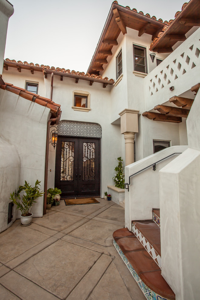 На фото: большая входная дверь в средиземноморском стиле с белыми стенами, бетонным полом, двустворчатой входной дверью и металлической входной дверью