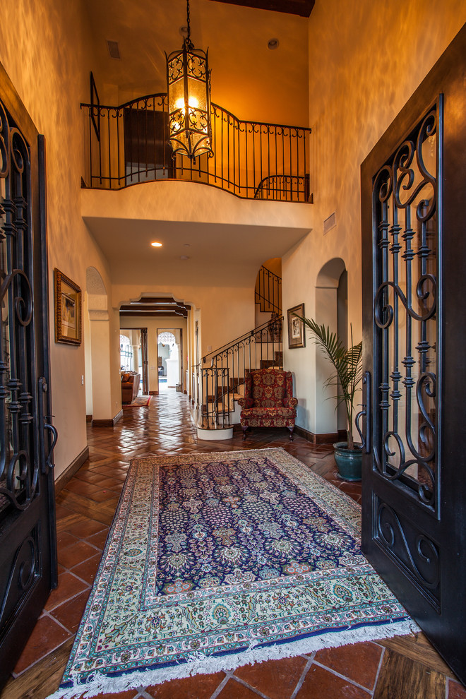 Example of a large tuscan terra-cotta tile and red floor entryway design in Santa Barbara with white walls and a metal front door