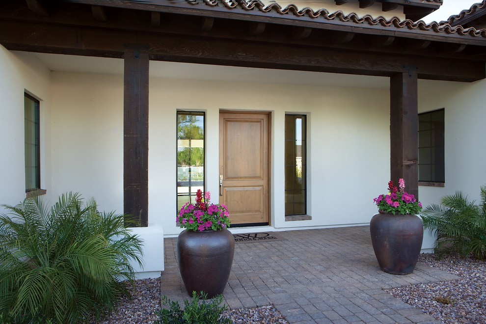 Ispirazione per una porta d'ingresso mediterranea di medie dimensioni con pareti bianche, una porta singola, una porta in legno chiaro e pavimento marrone