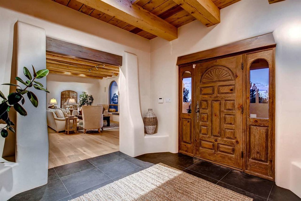 Idée de décoration pour un hall d'entrée sud-ouest américain avec une porte simple, une porte en bois brun, un mur blanc et un sol en ardoise.