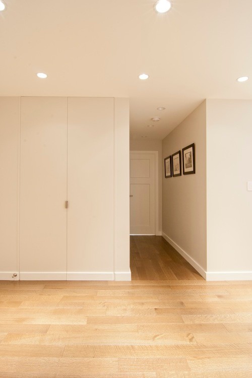 Modern inredning av en liten hall, med ljust trägolv, grå väggar, en enkeldörr, en vit dörr och beiget golv