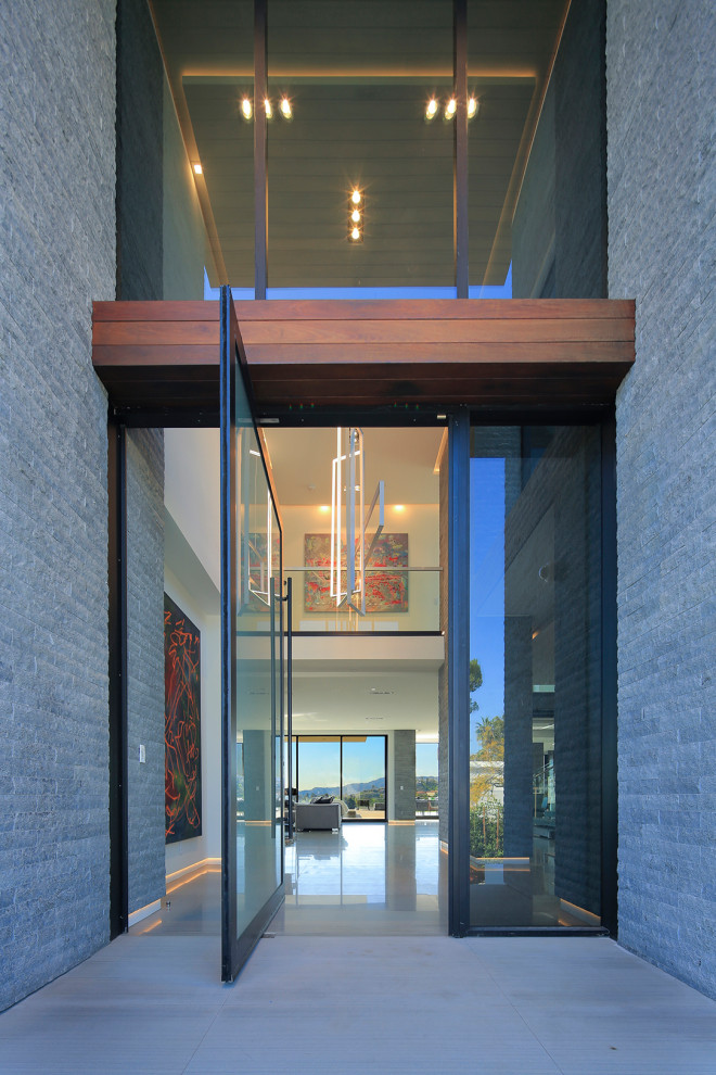 Réalisation d'une grande porte d'entrée design avec un mur gris, un sol en calcaire, une porte pivot, une porte en verre et un sol gris.