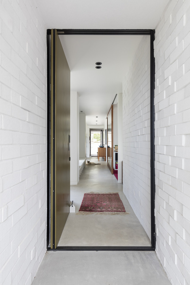 Inspiration pour une entrée minimaliste de taille moyenne avec un couloir, un mur blanc, sol en béton ciré, une porte pivot, une porte métallisée et un sol gris.