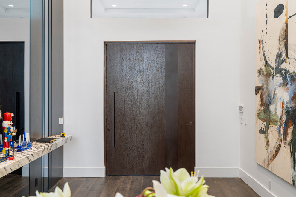Cette image montre une grande porte d'entrée design avec un mur blanc, un sol en bois brun, une porte pivot, une porte en bois foncé et un sol marron.