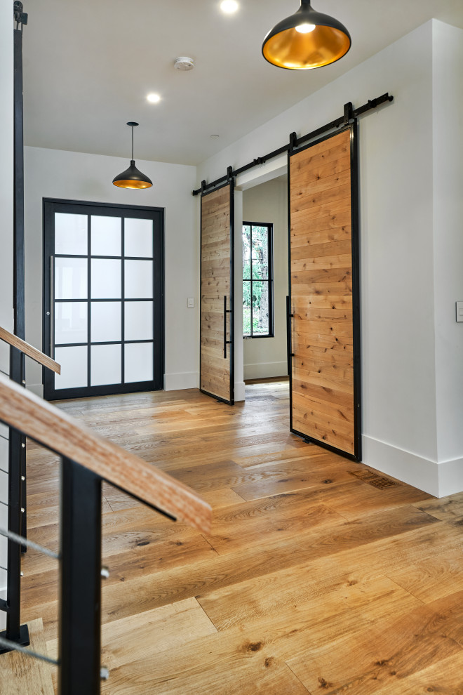 Réalisation d'une grande porte d'entrée minimaliste avec un mur gris, un sol en bois brun, une porte simple, une porte en verre et un sol marron.