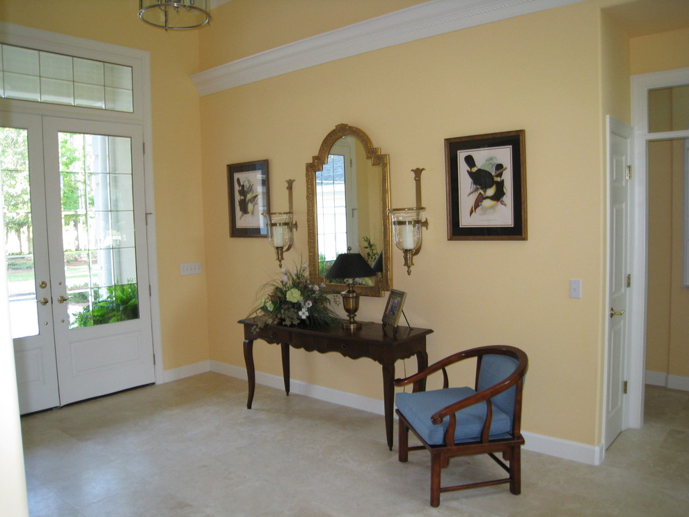 Пример оригинального дизайна: большое фойе в классическом стиле с желтыми стенами, полом из известняка, двустворчатой входной дверью и стеклянной входной дверью