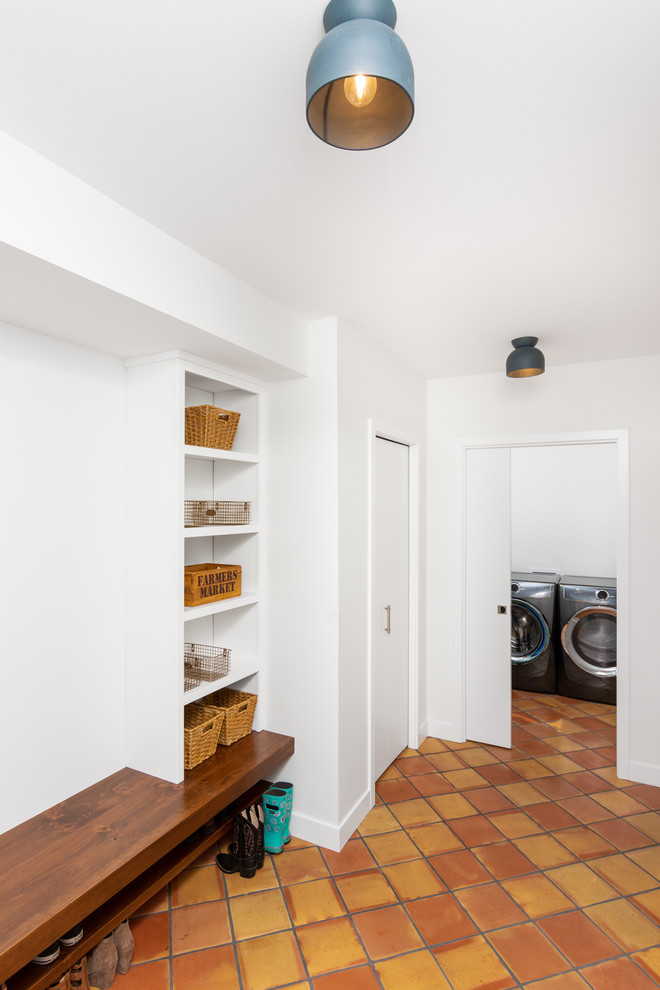 Réalisation d'une entrée minimaliste avec un vestiaire, un mur blanc, tomettes au sol et un sol orange.