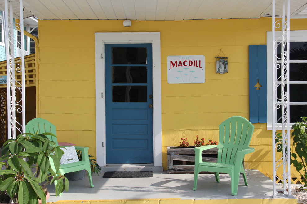 На фото: маленькая входная дверь в морском стиле с желтыми стенами, бетонным полом, одностворчатой входной дверью и синей входной дверью для на участке и в саду