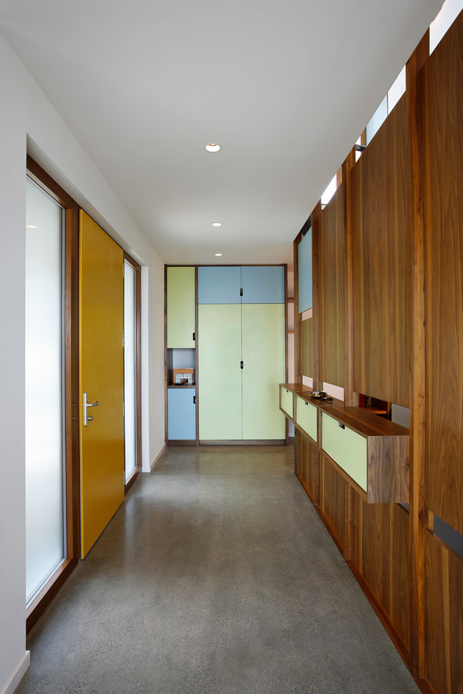 Cette image montre une entrée design avec sol en béton ciré, une porte simple et une porte jaune.