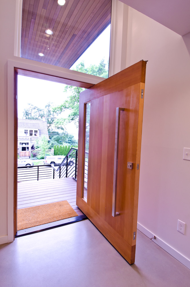 Foto de puerta principal minimalista de tamaño medio con paredes blancas, suelo de cemento, puerta pivotante y puerta de madera en tonos medios