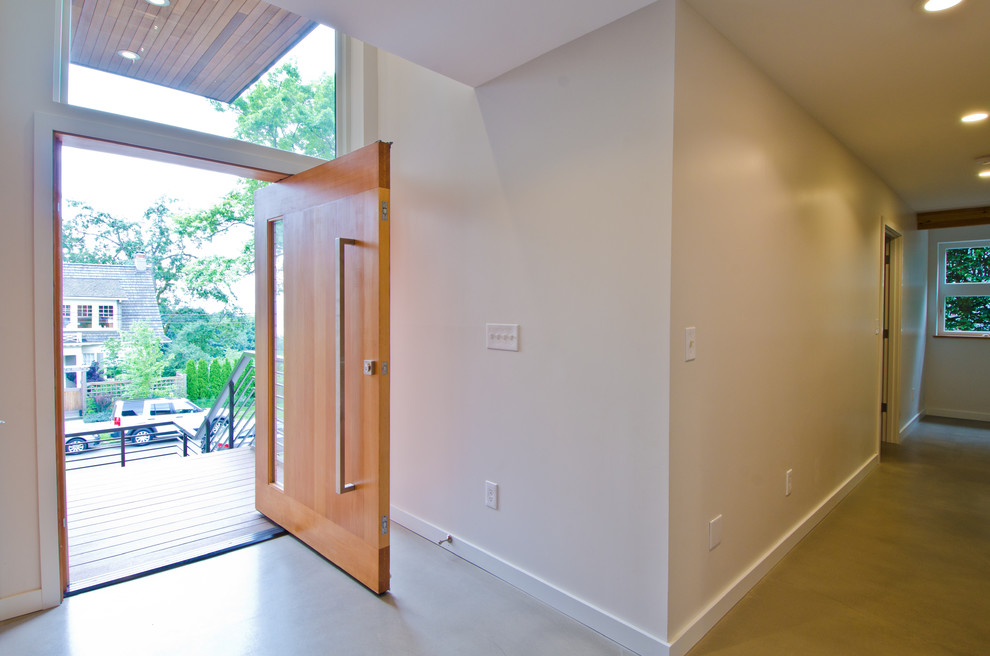 Ispirazione per un grande ingresso moderno con pareti beige, pavimento in cemento, una porta a pivot e una porta in legno chiaro