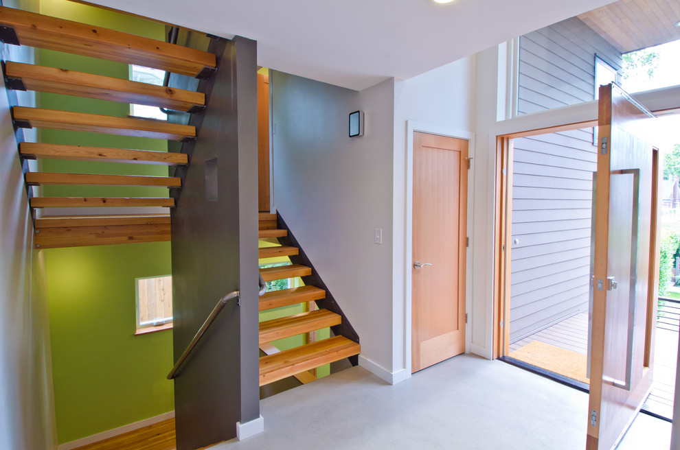 На фото: большое фойе в стиле модернизм с бежевыми стенами, поворотной входной дверью, входной дверью из светлого дерева и бетонным полом с