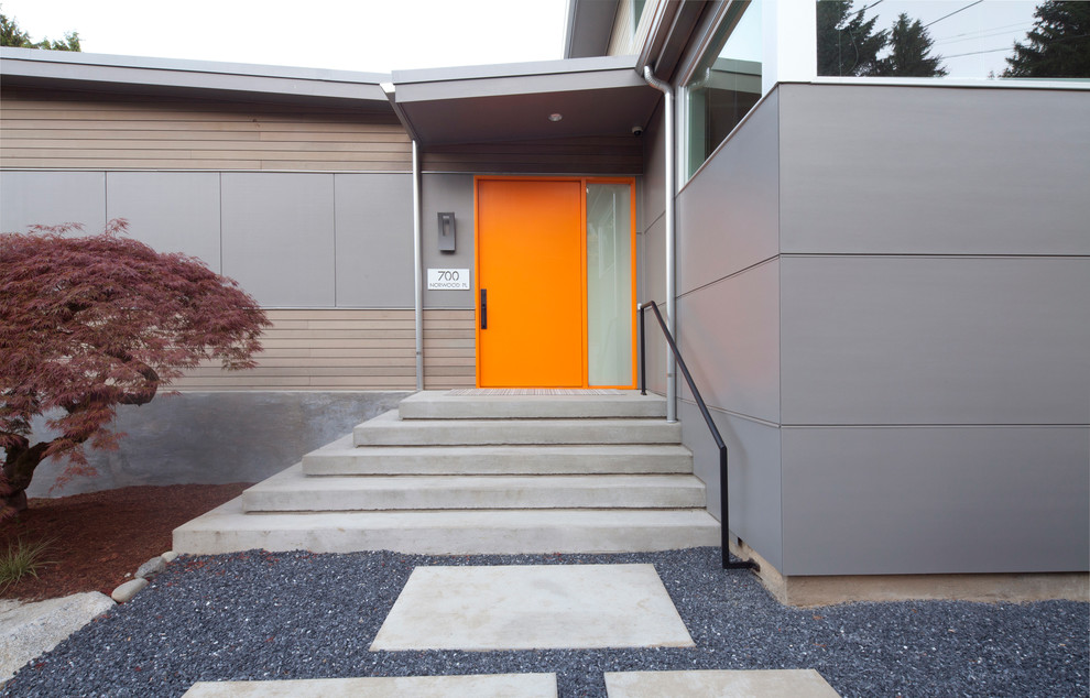 Bild på en mellanstor funkis ingång och ytterdörr, med grå väggar, betonggolv, en pivotdörr och en orange dörr