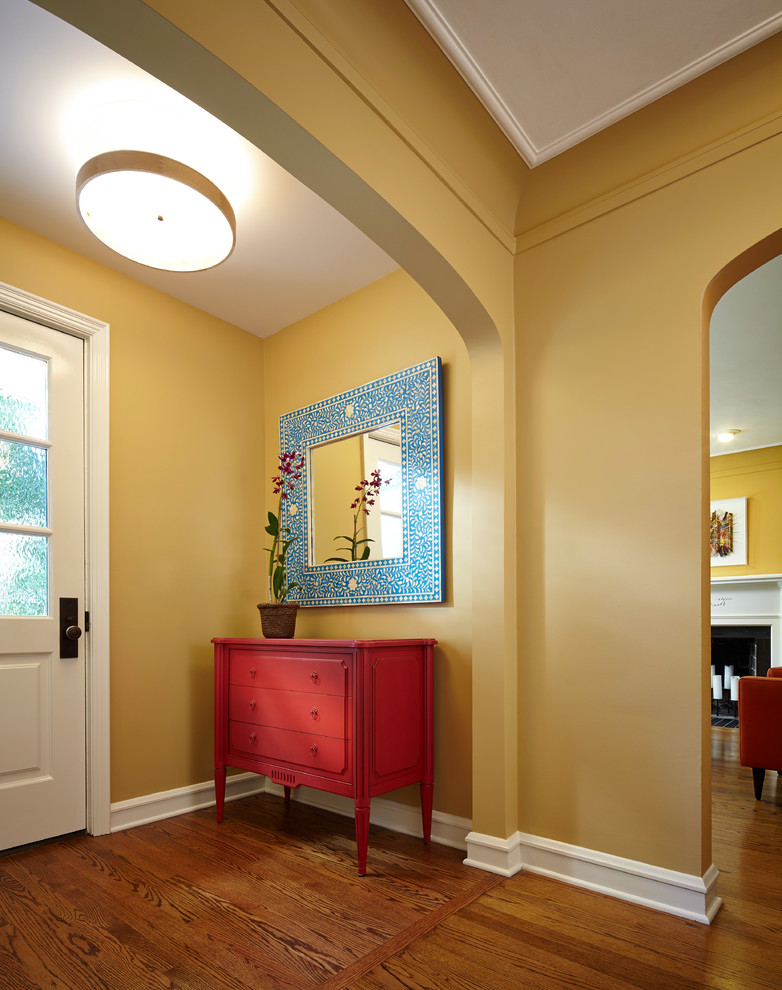 Aménagement d'un hall d'entrée classique avec un mur jaune, un sol en bois brun, une porte simple et une porte blanche.
