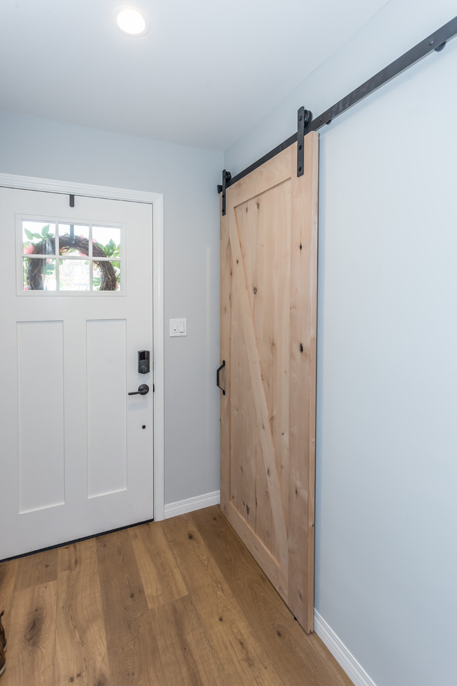 Bild på en mellanstor lantlig ingång och ytterdörr, med blå väggar, mellanmörkt trägolv, en enkeldörr, en vit dörr och brunt golv