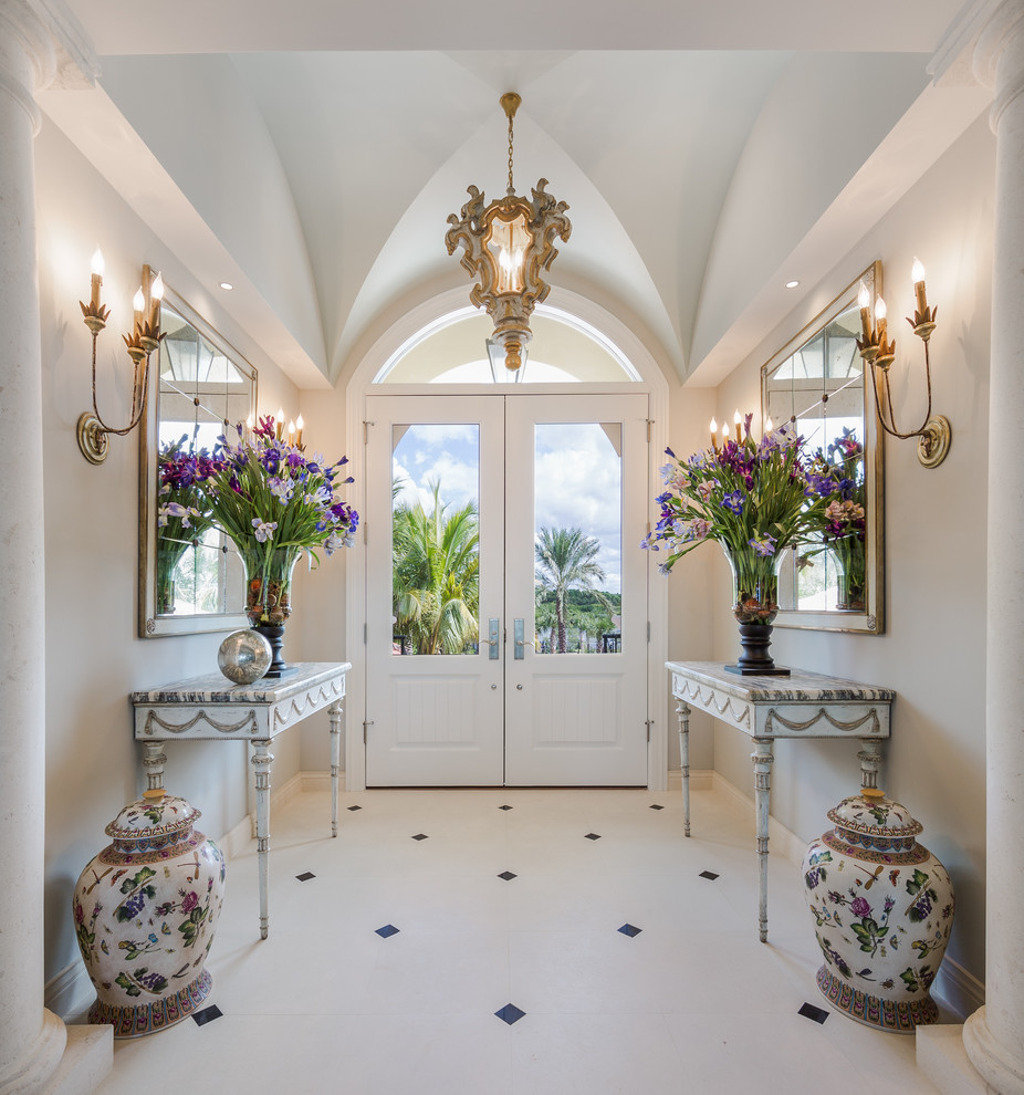 タンパにあるラグジュアリーなトラディショナルスタイルのおしゃれな玄関ロビー (グレーの壁、ライムストーンの床、白いドア) の写真