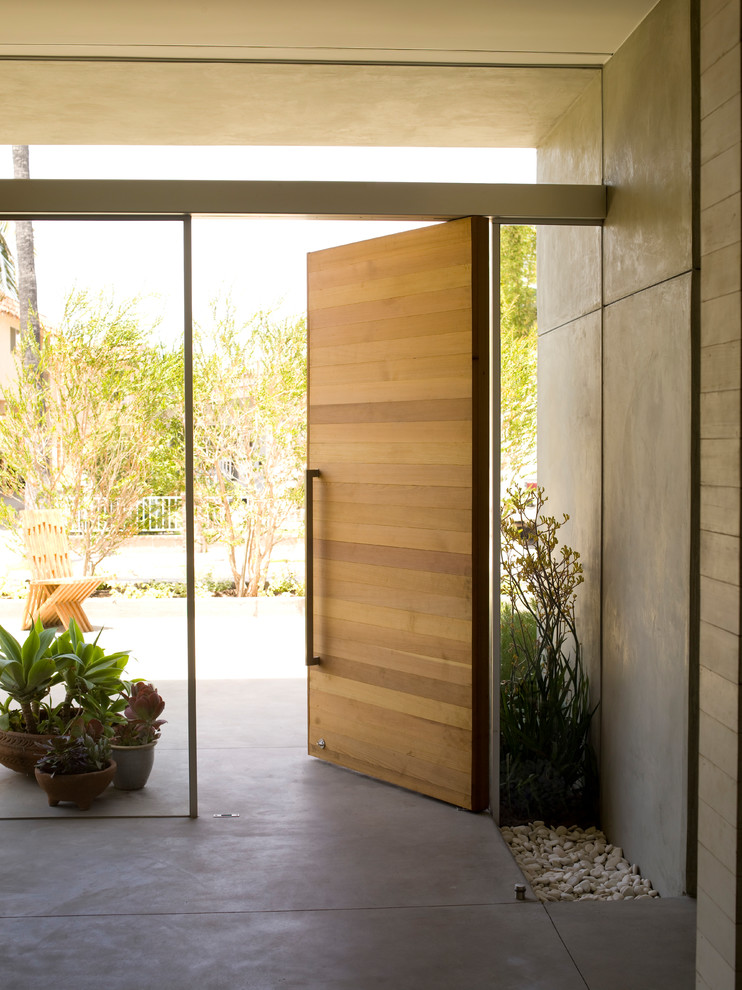 На фото: фойе среднего размера в стиле модернизм с белыми стенами, бетонным полом, поворотной входной дверью, входной дверью из дерева среднего тона и серым полом