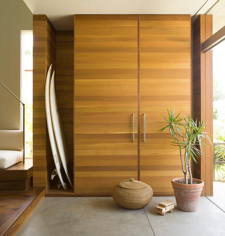 Imagen de distribuidor moderno de tamaño medio con paredes blancas, suelo de cemento, puerta pivotante, puerta de madera en tonos medios y suelo gris