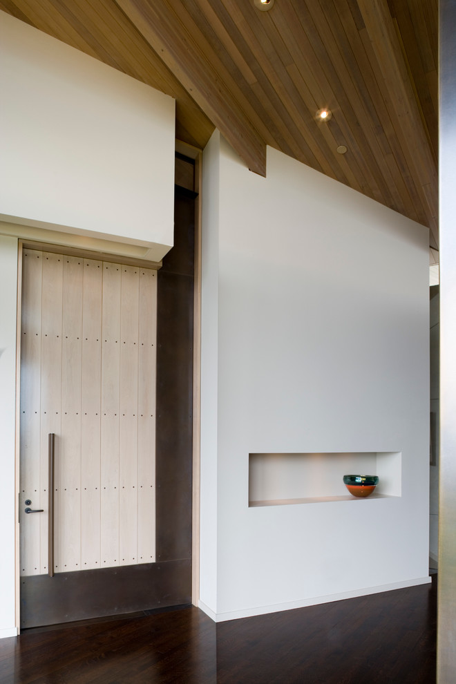 На фото: фойе среднего размера в современном стиле с белыми стенами, темным паркетным полом, поворотной входной дверью и входной дверью из светлого дерева