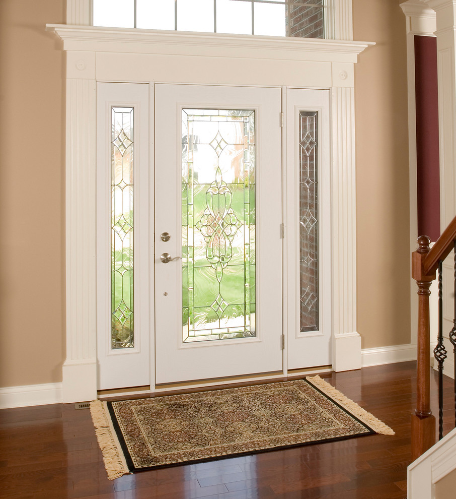 Klassisk inredning av en stor ingång och ytterdörr, med en enkeldörr, beige väggar, mörkt trägolv, en vit dörr och brunt golv