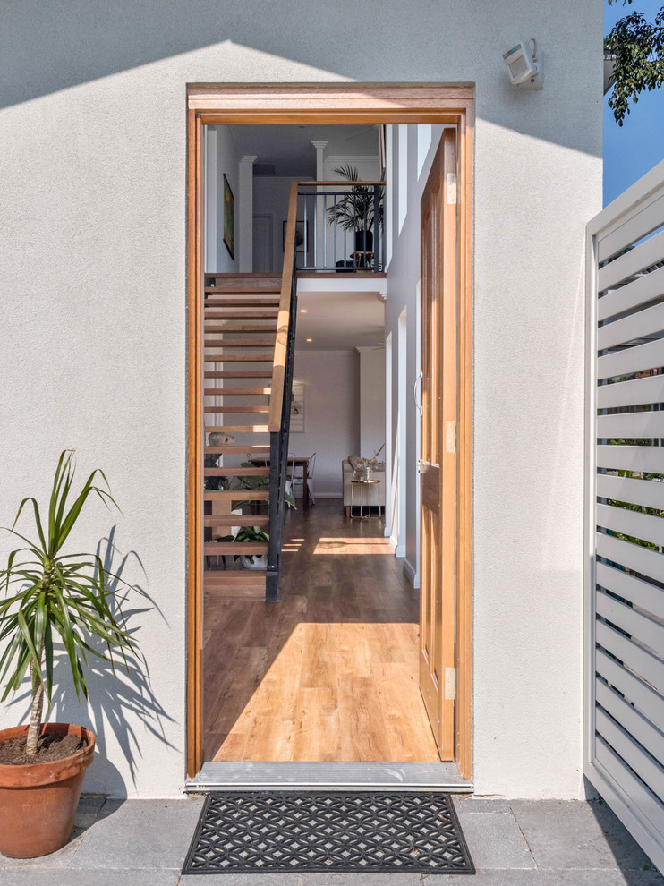 Ejemplo de puerta principal contemporánea pequeña con paredes blancas, suelo laminado, puerta simple, puerta de madera clara y suelo marrón