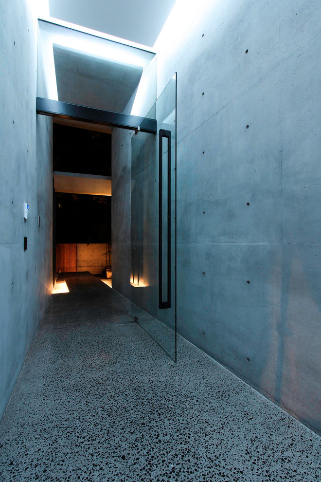 Bild på en mellanstor funkis ingång och ytterdörr, med svarta väggar, betonggolv, en pivotdörr, glasdörr och grått golv