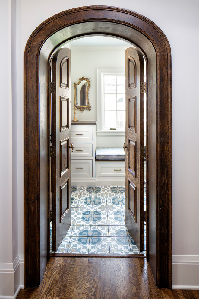 Idée de décoration pour une entrée méditerranéenne avec un vestiaire, un mur blanc, un sol en carrelage de céramique, une porte marron et un sol bleu.