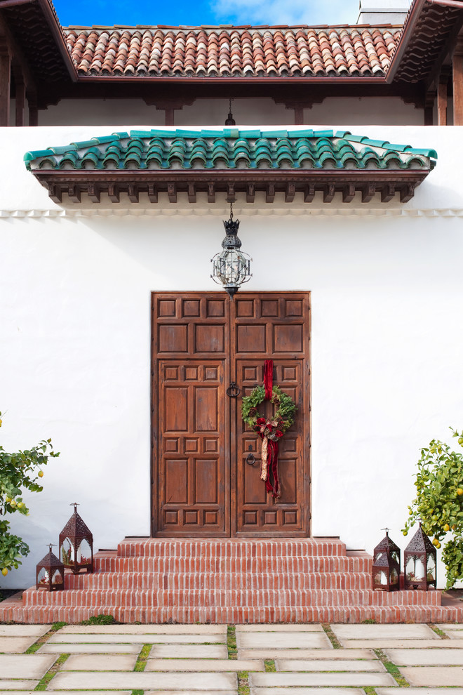 Modelo de puerta principal mediterránea con paredes blancas, puerta doble y puerta de madera en tonos medios