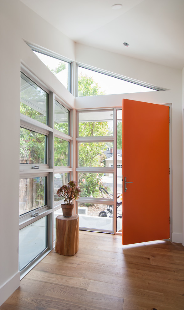 This is an example of a medium sized contemporary front door in San Francisco with white walls, light hardwood flooring, a single front door and an orange front door.