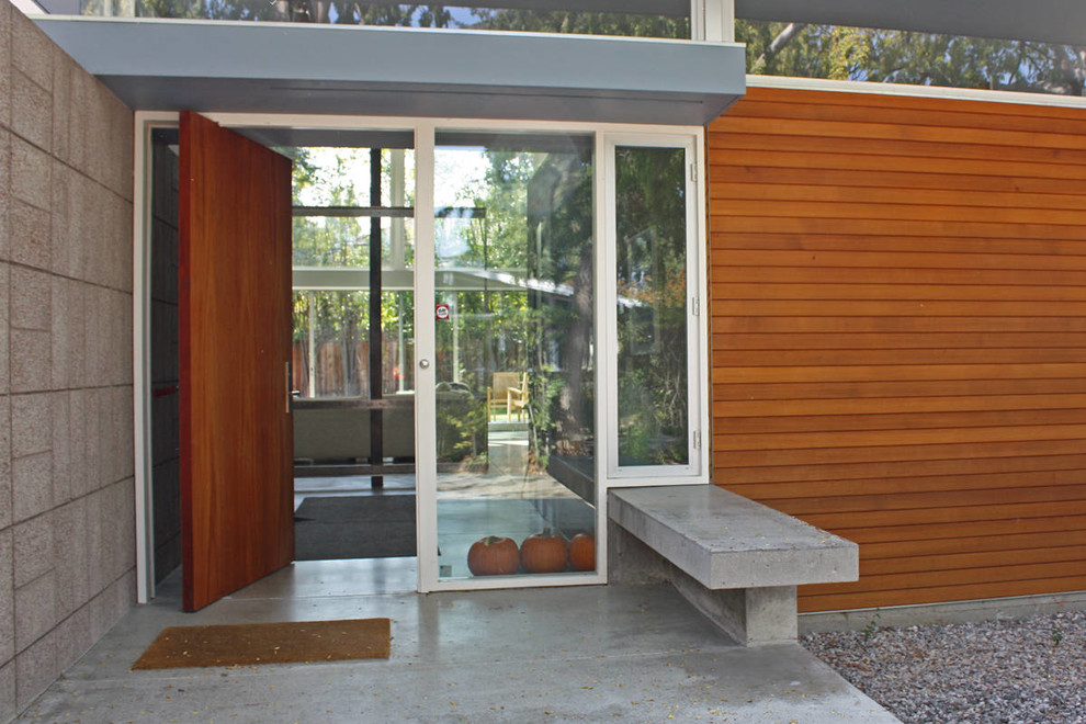 Foto di una grande porta d'ingresso minimalista con pareti grigie, pavimento in cemento, una porta a pivot e una porta in legno bruno