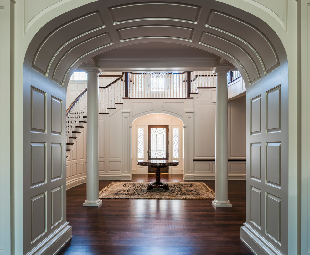 Cette image montre un hall d'entrée traditionnel de taille moyenne avec un mur blanc, parquet foncé, une porte simple, une porte en bois foncé et un sol marron.