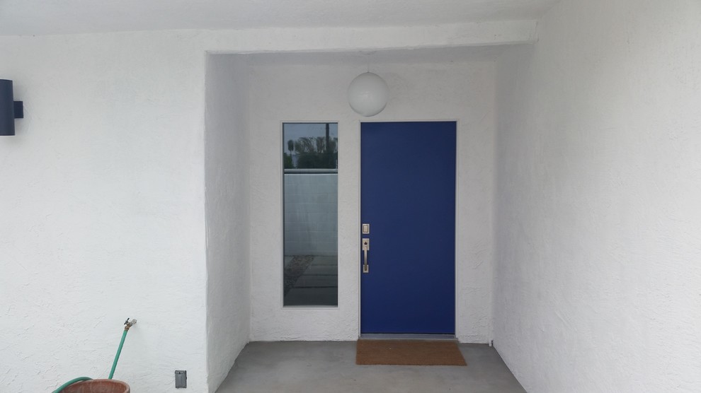 Imagen de puerta principal vintage con paredes blancas, suelo de cemento, puerta simple y puerta azul