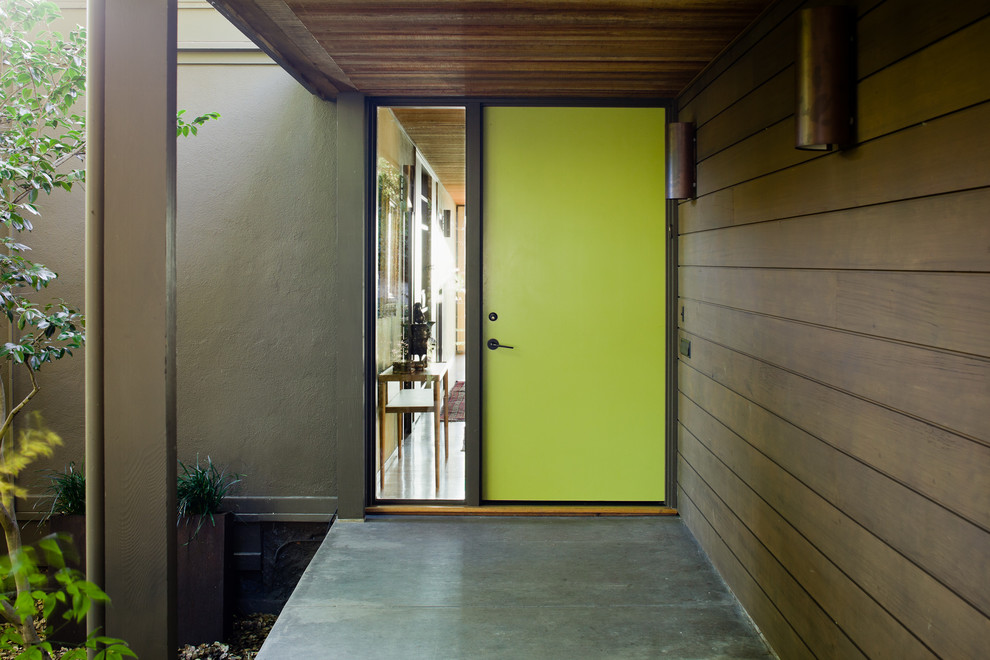 60 tals inredning av en stor ingång och ytterdörr, med bruna väggar, betonggolv, en enkeldörr och en grön dörr
