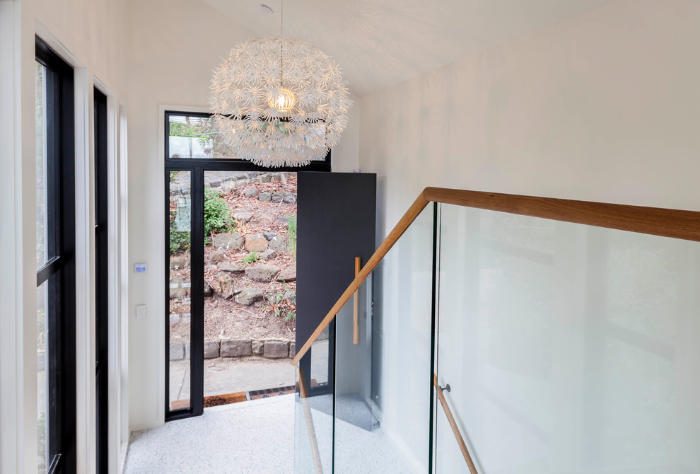 メルボルンにあるラグジュアリーな広いミッドセンチュリースタイルのおしゃれな玄関ドア (白い壁、テラゾーの床、黒いドア) の写真