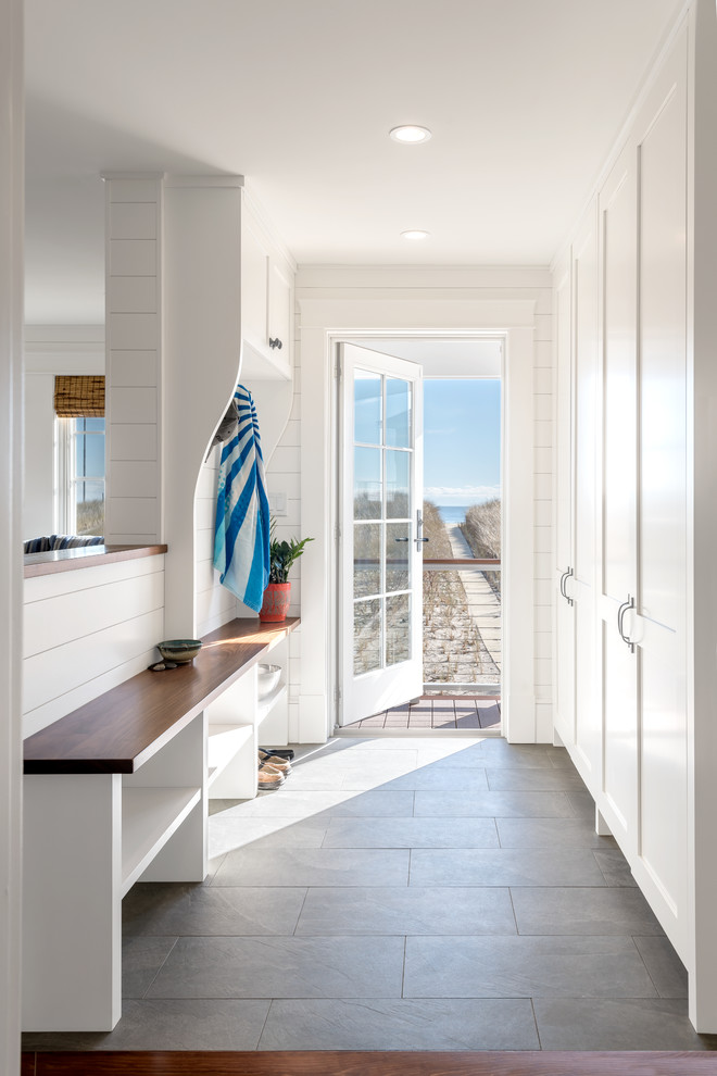 Aménagement d'une entrée bord de mer avec un vestiaire, un mur blanc, une porte simple, une porte en verre et un sol gris.