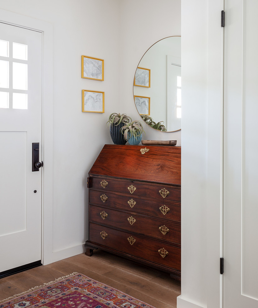 На фото: узкая прихожая в стиле неоклассика (современная классика) с белыми стенами, одностворчатой входной дверью, белой входной дверью, паркетным полом среднего тона и коричневым полом с