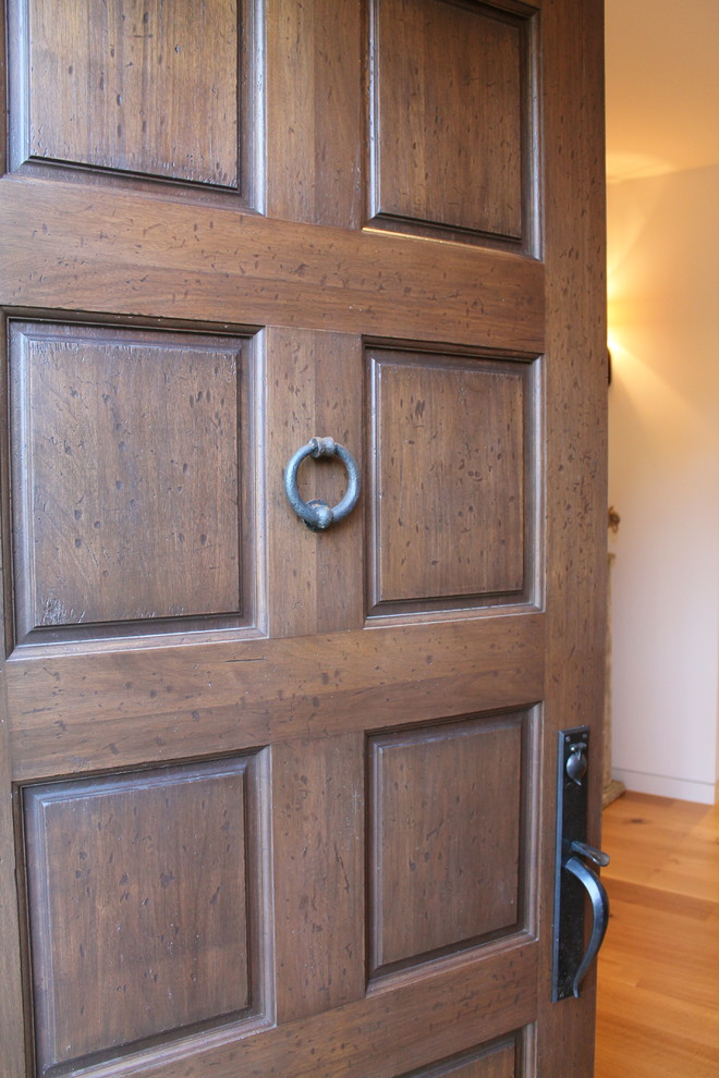 Modelo de puerta principal mediterránea con paredes blancas, suelo de madera clara, puerta simple y puerta de madera en tonos medios