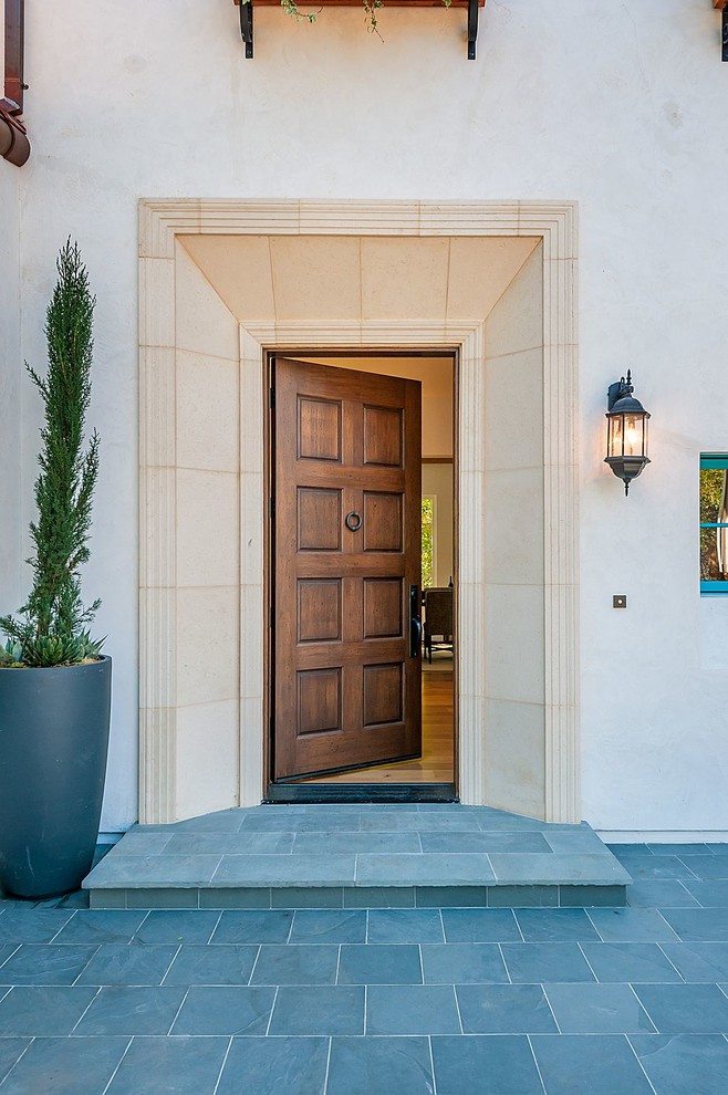 Modelo de puerta principal mediterránea grande con paredes blancas, suelo de pizarra, puerta simple y puerta de madera en tonos medios
