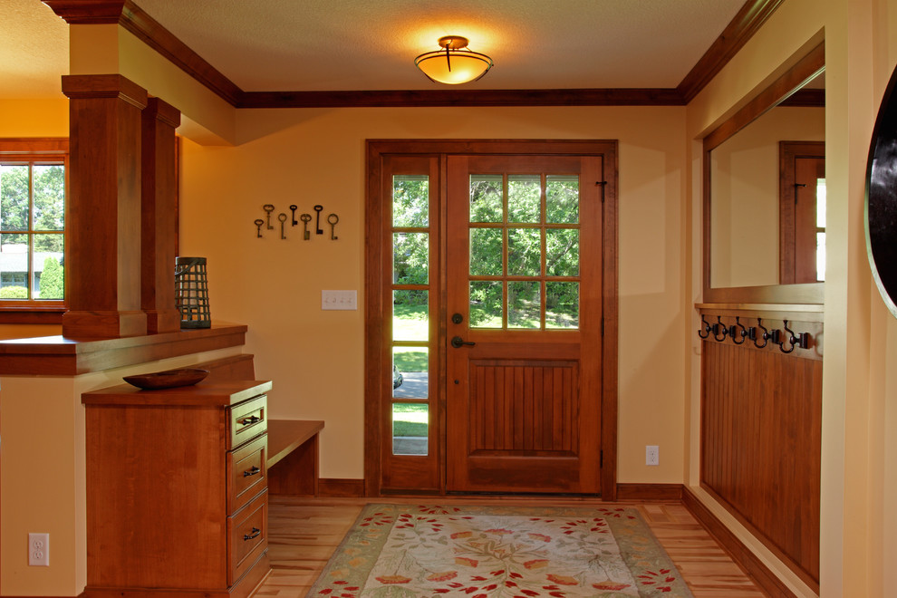 Cette image montre une porte d'entrée traditionnelle avec un mur jaune, parquet clair, une porte simple et une porte en bois brun.