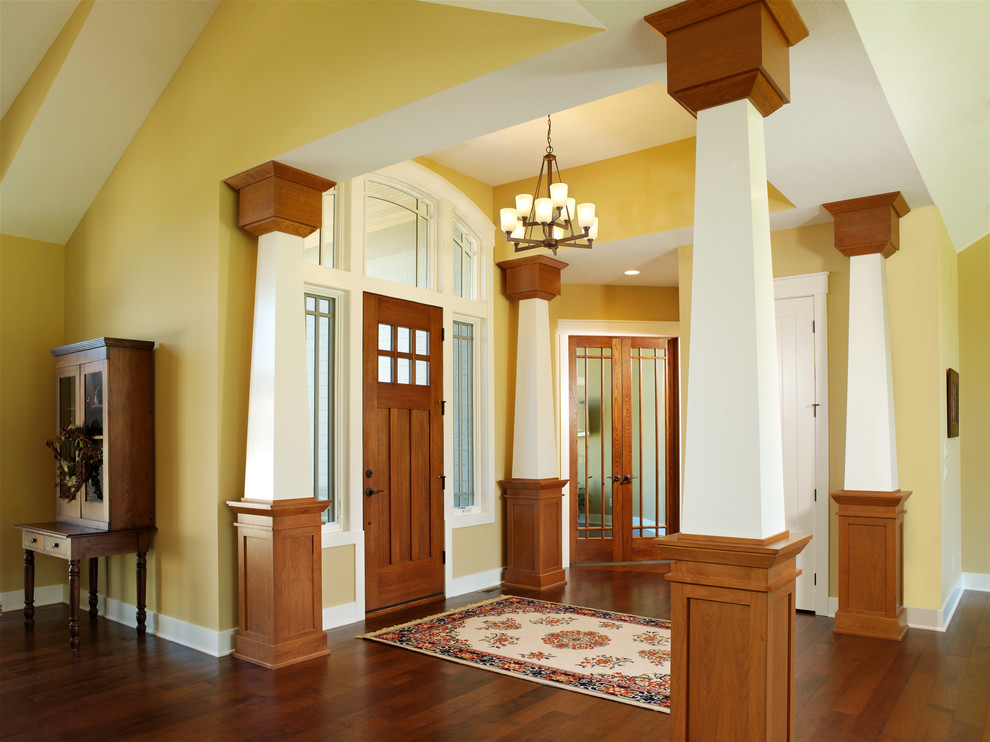 Cette image montre une porte d'entrée craftsman de taille moyenne avec un mur jaune, parquet foncé, une porte simple et une porte en bois brun.