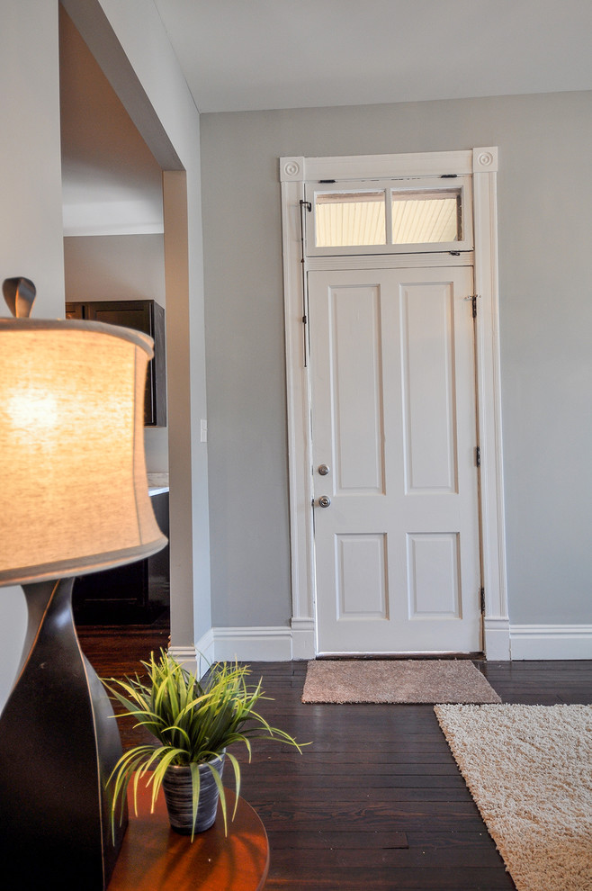 Modelo de entrada clásica con paredes grises, suelo de madera en tonos medios, puerta simple y puerta blanca