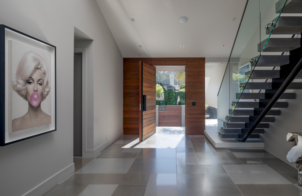 Diseño de distribuidor minimalista grande con paredes grises, suelo de cemento, puerta pivotante, puerta de madera en tonos medios y suelo gris
