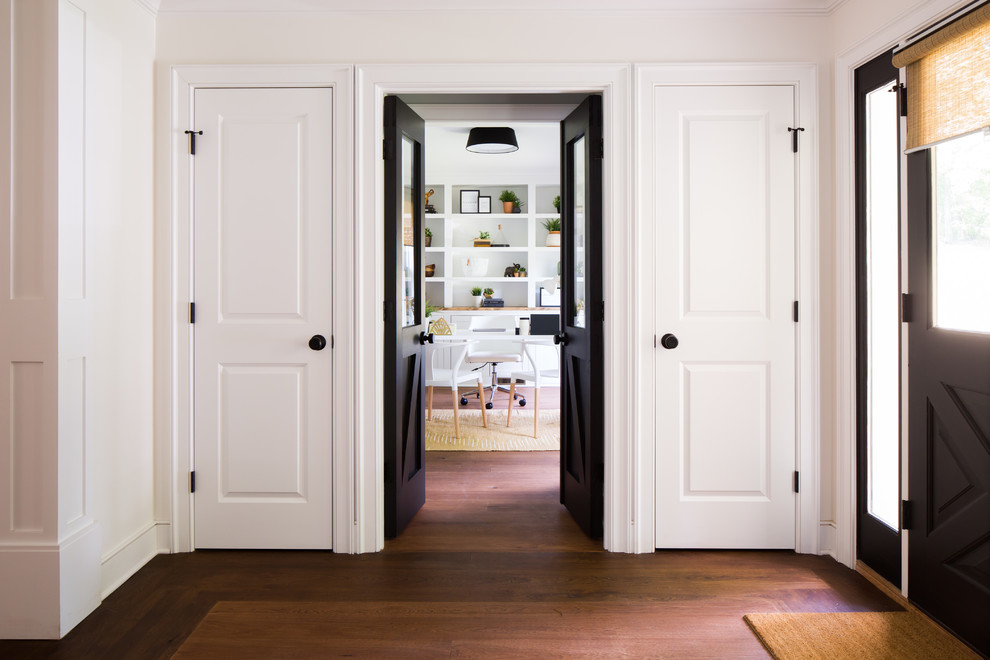 Aménagement d'un grand hall d'entrée classique avec un mur blanc, un sol en bois brun, une porte simple, une porte noire et un sol marron.