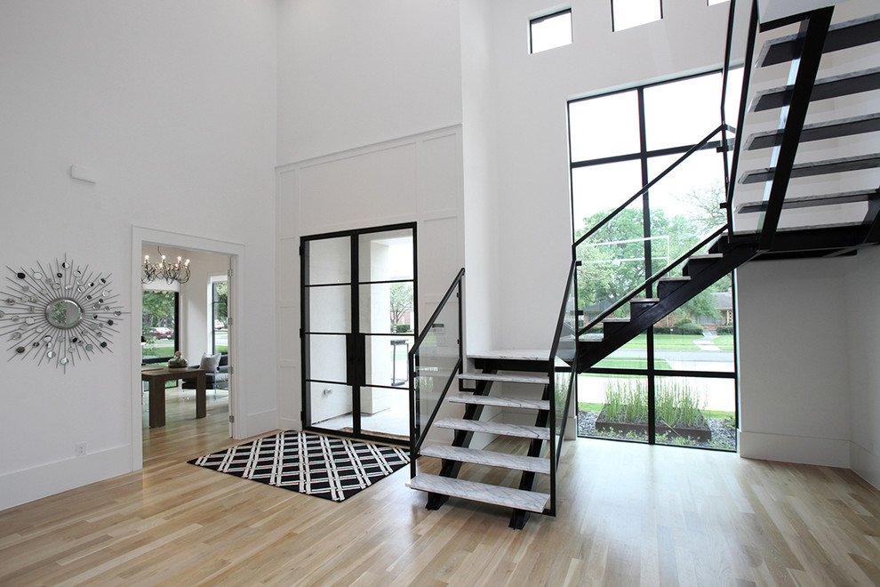 Foto på en stor funkis foajé, med vita väggar, ljust trägolv, en dubbeldörr, en svart dörr och beiget golv
