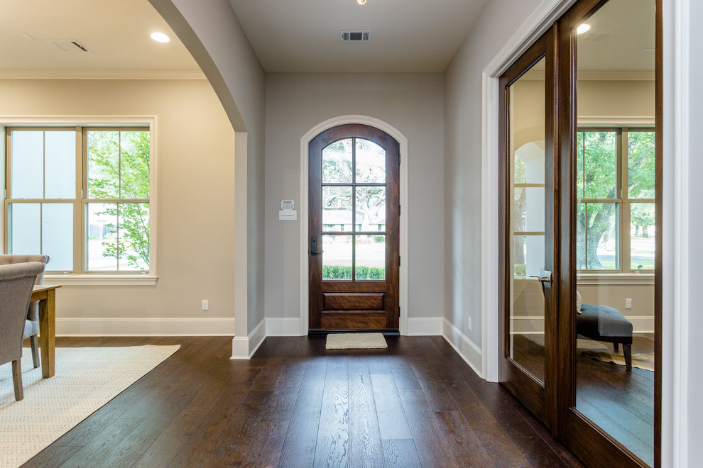Cette photo montre un grand hall d'entrée tendance avec un mur gris, parquet foncé, une porte simple, une porte en bois brun et un sol marron.