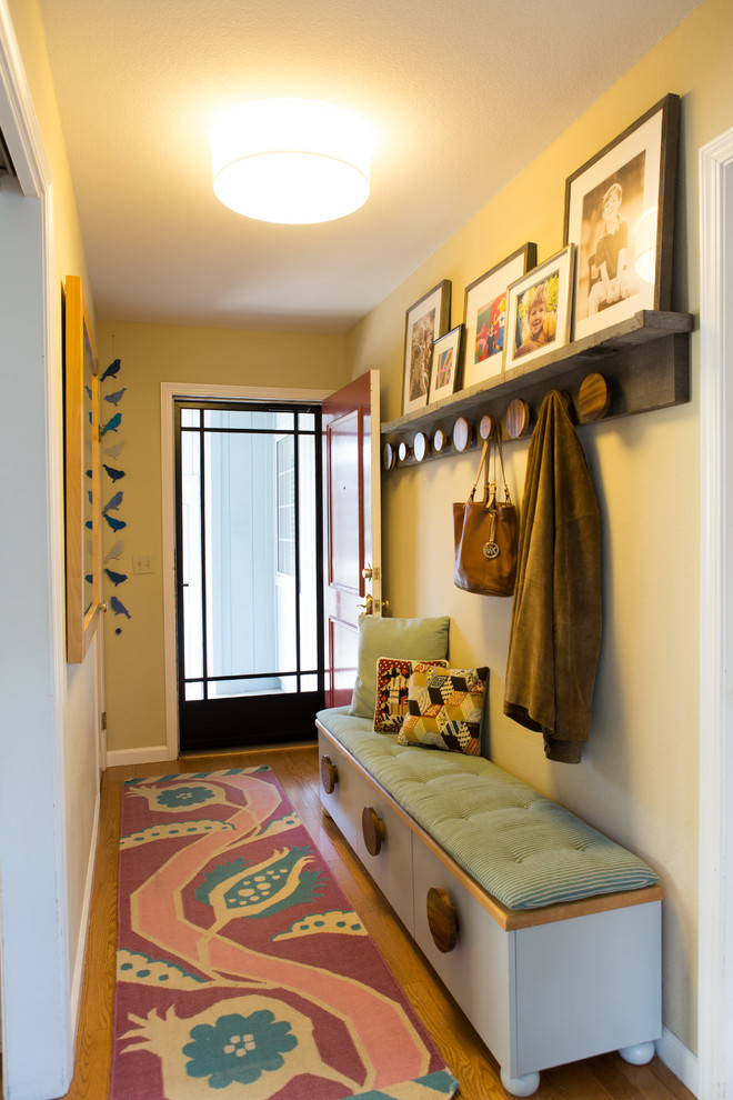 Cette photo montre une petite entrée moderne avec un couloir, un mur beige, un sol en bois brun, une porte simple et une porte rouge.