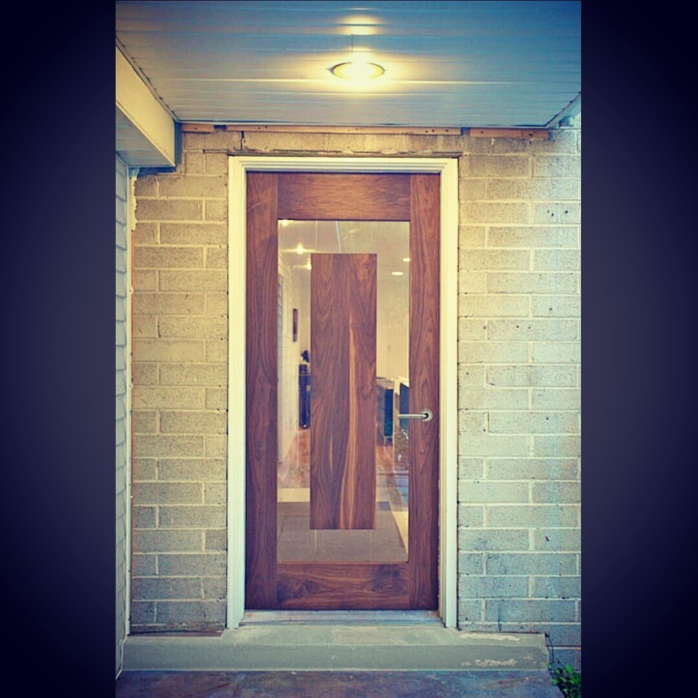 Réalisation d'une porte d'entrée minimaliste de taille moyenne avec une porte simple, un mur blanc, une porte en bois brun et sol en béton ciré.